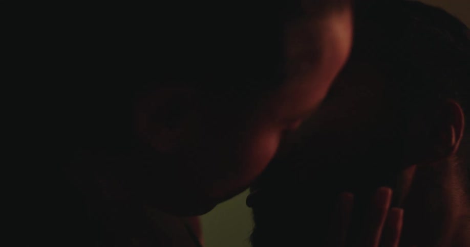 An intimate close-up shows a couple in silhouette kissing and caressing each other with passion