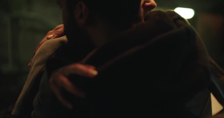 An emotional young woman cries while hugging and kissing a man in a dimly lit setting at night