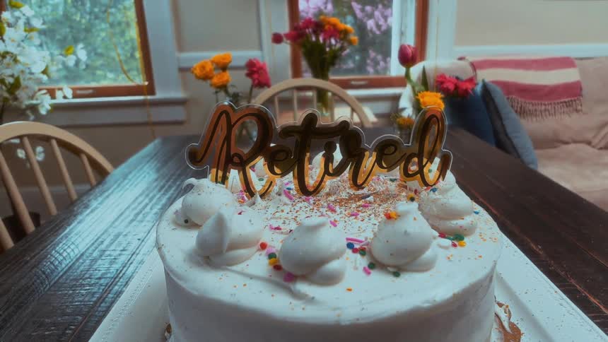 A festive cake with a golden 'Retired' topper and colorful sprinkles is the centerpiece of a retirement party
