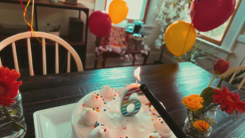 A slow-motion, first-person view of lighting the number six candle on a birthday cake, which is then blown out
