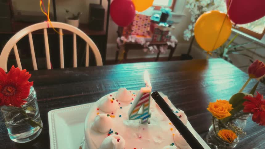 A slow-motion point-of-view shot of a lighter igniting the number four candle on a festive birthday cake
