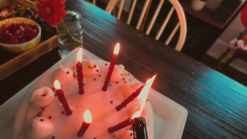 A slow pullback from a close-up of a festive birthday cake with lit candles reveals a beautifully arranged party table