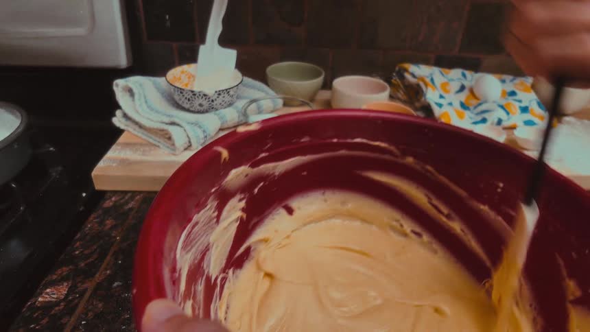 Close-up, first-person perspective of mixing creamy cake batter with a spatula in a red bowl