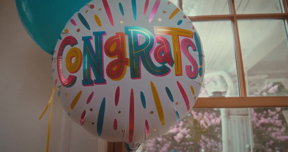 A festive 'Congrats!' balloon for a celebration gently sways in front of a bright window