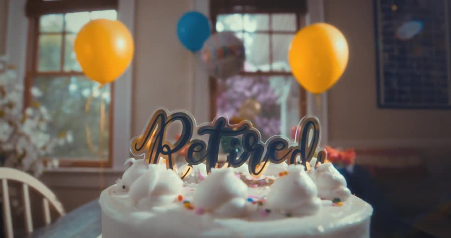 A retirement party cake with a celebratory 'Retired' sign sits on a table, with festive balloons in the background