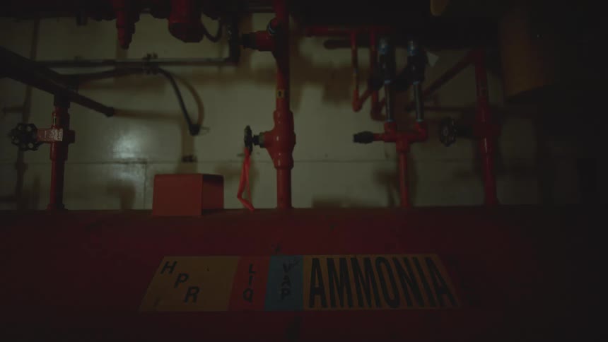 A flashing red alarm light illuminates an ammonia tank and pipes in a dark, industrial engine room
