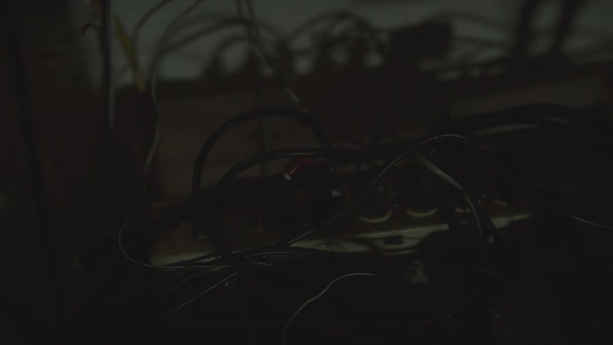 A tangled mess of electronic cables plugged into a power strip flashes ominously under a red light