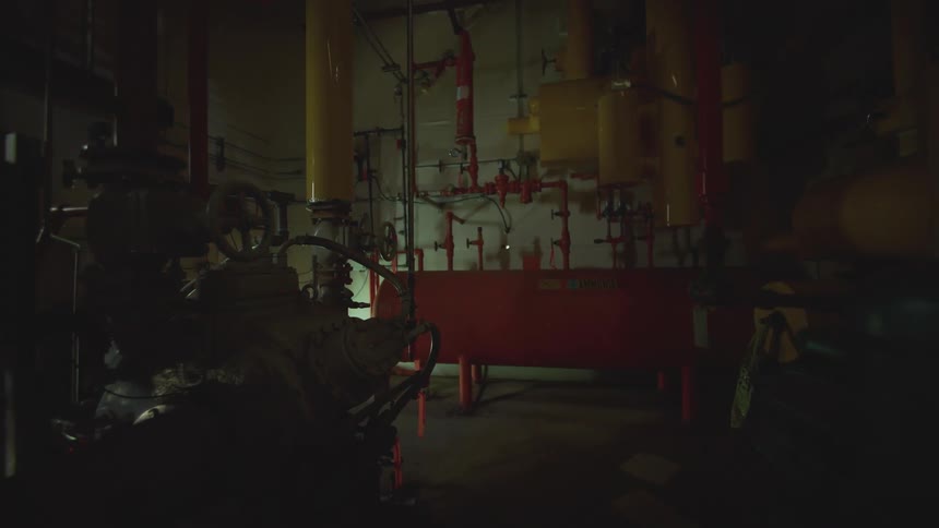 A slow pull back shot of a creepy industrial basement with pipes and valves under a flashing red warning light