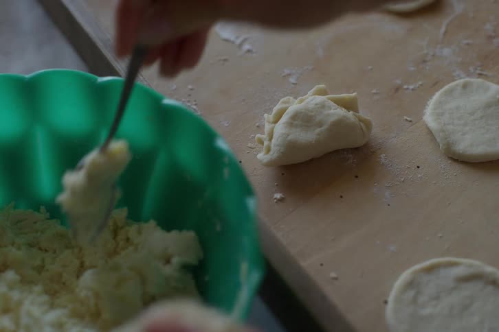 A person's hands carefully prepare homemade dumplings in slow motion, scooping filling into the dough on a wooden board