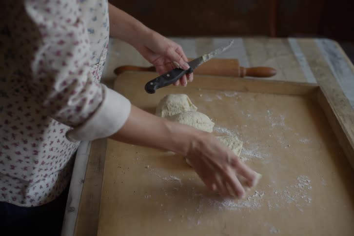Slow motion close-up of a woman's hands cutting dough into portions on a rustic wooden board