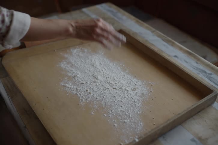 A baker sprinkles flour onto a rustic wooden board in slow motion before starting to bake