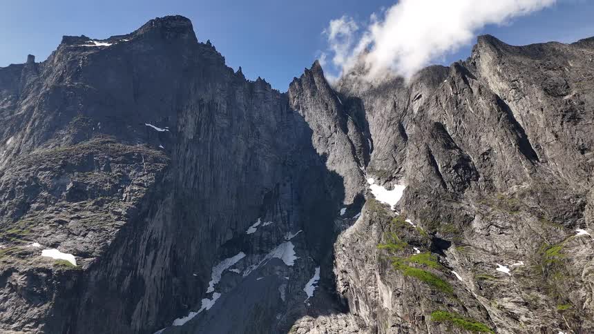 A stunning low-angle view of a dramatic, rocky mountain range with lingering snow patches against a bright blue sky