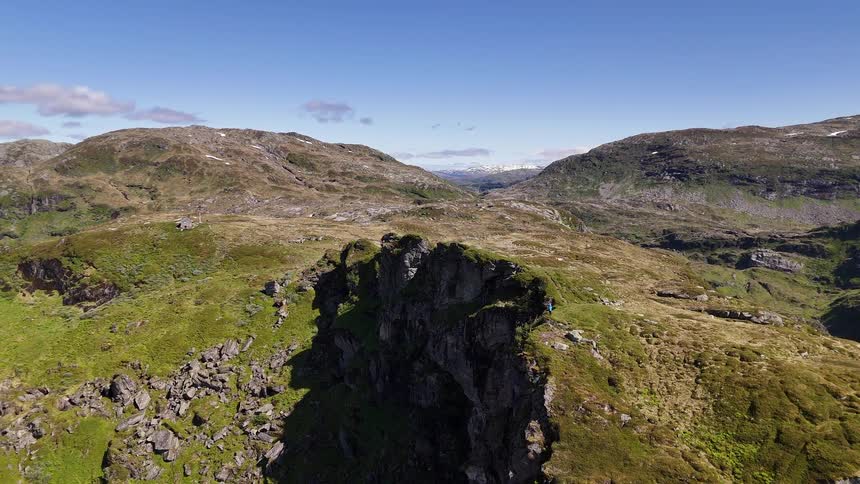 Epic aerial pullback reveals a lone hiker and their tent perched on a dramatic cliff in a vast, rugged mountain wilderness