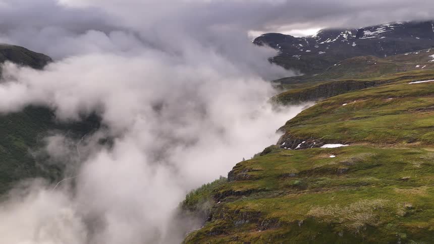 A slow, majestic pullback shot reveals a deep mountain valley shrouded in a sea of thick, rolling clouds under an overcast sky