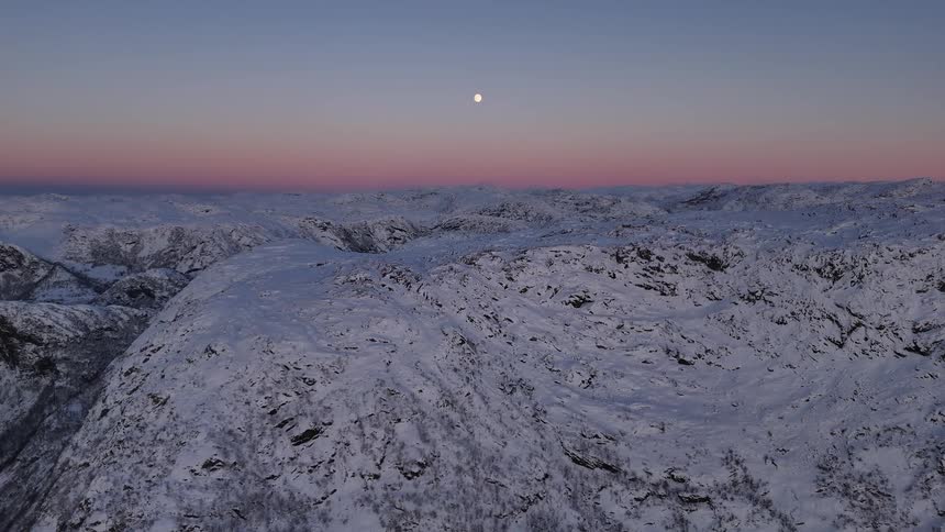 A beautiful full moon hangs in the pink and blue twilight sky over a vast, frozen mountain landscape