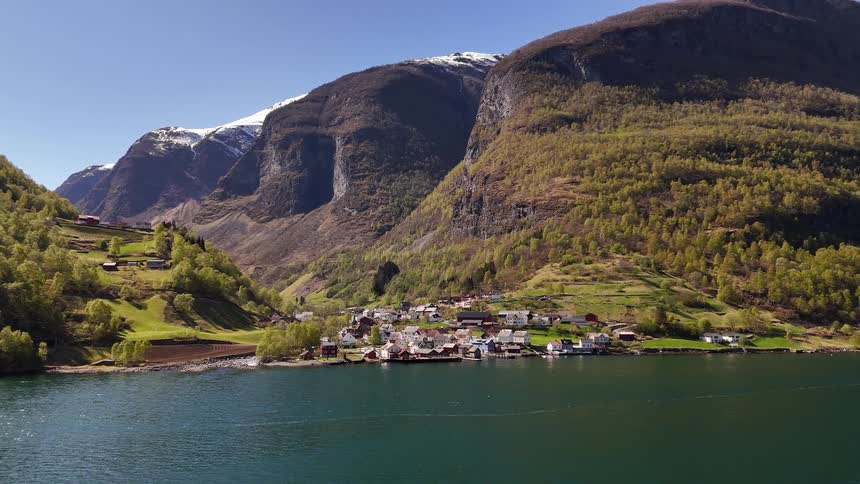 A tranquil village is nestled on the shore of a majestic Norwegian fjord, with snow-capped mountains rising into a clear blue sky