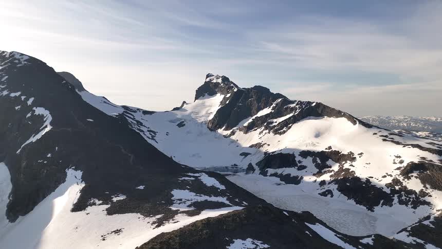 An epic aerial view slowly pulls back from a majestic, snow-capped mountain range revealing a glacier and frozen alpine lake