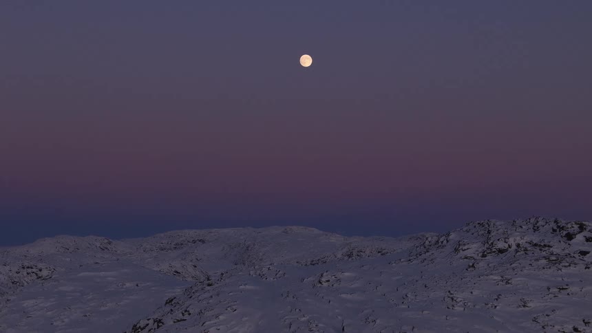 A serene full moon shines brightly in the purple twilight sky over a vast, snow-covered mountain landscape