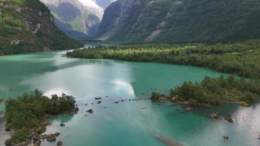 Spectacular aerial pullback reveals a vibrant turquoise glacial lake and a massive glacier nestled between towering green mountains