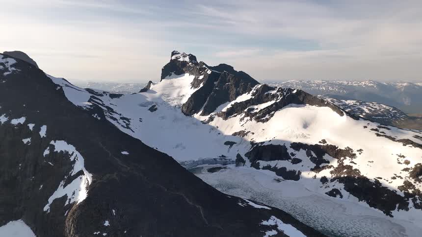 An expansive aerial shot pulls back to reveal a stunning snow-capped mountain range and a partially frozen glacial lake