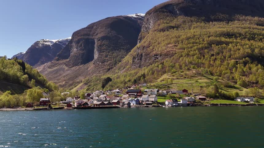 A breathtaking view of a picturesque village nestled on the shoreline of a Norwegian fjord, surrounded by majestic, snow-capped mountains