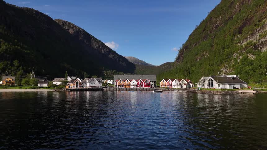 A serene aerial view of a colorful coastal village nestled between mountains on a calm fjord in Norway