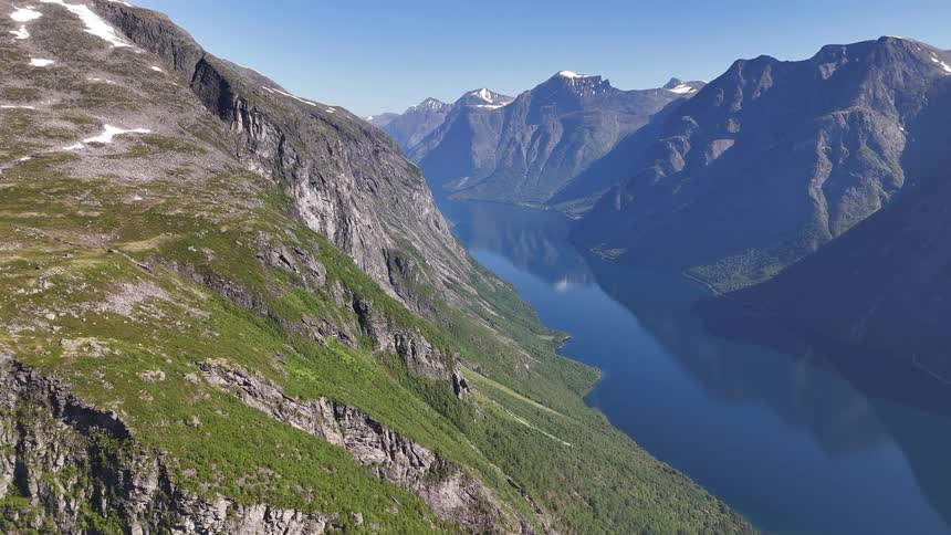 A majestic aerial view of a deep blue fjord winding through snow-capped mountains in Norway on a clear summer day