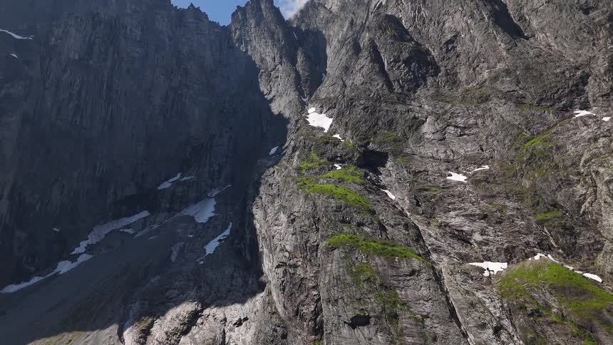 A dramatic aerial view slowly tilts up the immense, rugged rock face of the Trollveggen mountain range in Norway