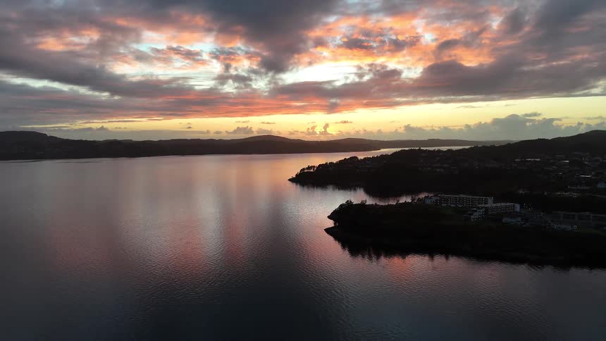 A stunning aerial view captures a vibrant sunset painting the clouds and reflecting on the calm waters of a bay