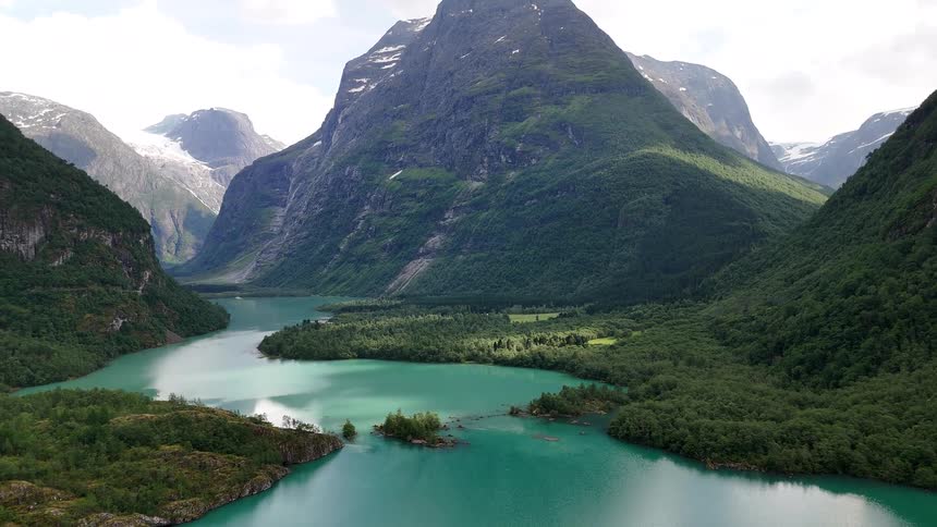 Spectacular aerial footage reveals a turquoise glacial lake winding through a majestic valley surrounded by towering green mountains