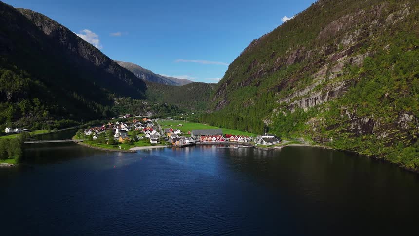 A serene aerial view of a picturesque Norwegian village nestled between steep mountains and a calm fjord on a sunny day