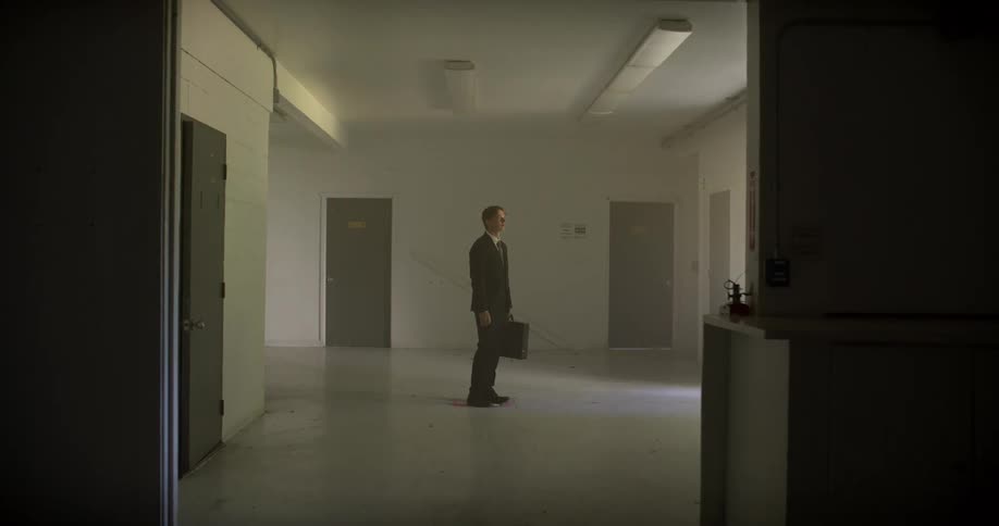 A lone businessman in a suit walks through a stark, empty institutional hallway