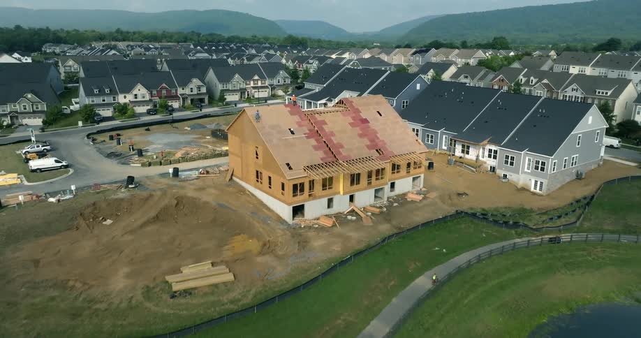 A slow aerial push-in reveals roofers working on a new townhome in a large suburban neighborhood development