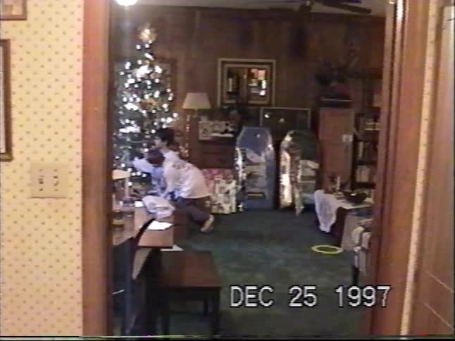 Vintage VHS footage captures a family gathering around the Christmas tree to open presents on Christmas morning in 1997
