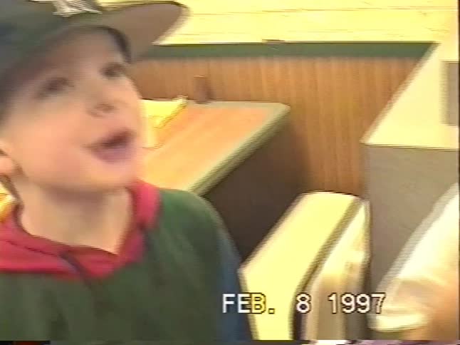 A vintage 1997 home video captures a young boy eating and looking around in a fast-food restaurant