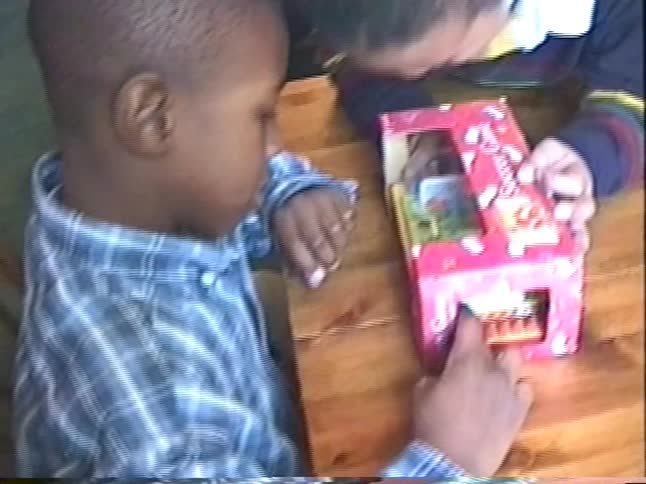 Two young boys curiously inspect a new tabletop soccer game together at a wooden table in this vintage footage