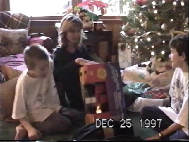 A mother and her two sons gather around the Christmas tree to open a big present on Christmas morning in 1997