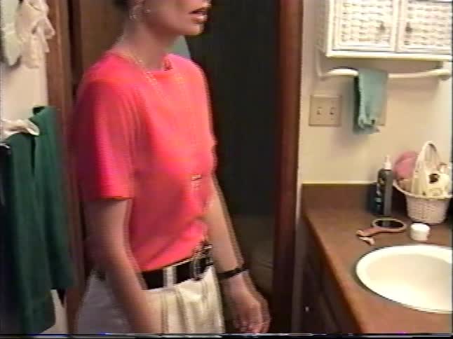 Vintage home video footage shows a woman putting on a necklace while getting ready in the bathroom