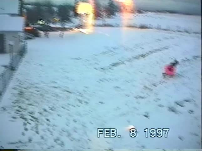Nostalgic home video of a person sledding down a snowy hill on a pink inflatable tube in 1997