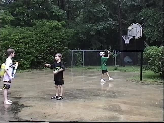 Nostalgic VHS footage captures carefree kids playing basketball and with water guns on a rainy summer day