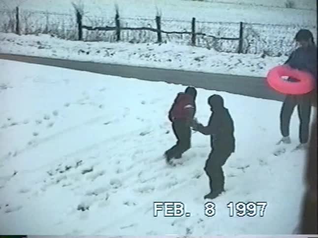 Vintage 1997 footage of a father and his children enjoying a winter day, playing and sledding together in the snow