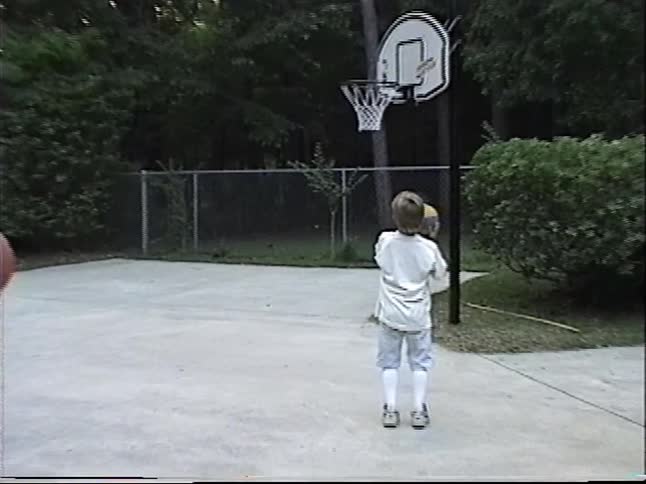 A father teaches his two sons some basketball tricks in the driveway in this fun 1990s home video