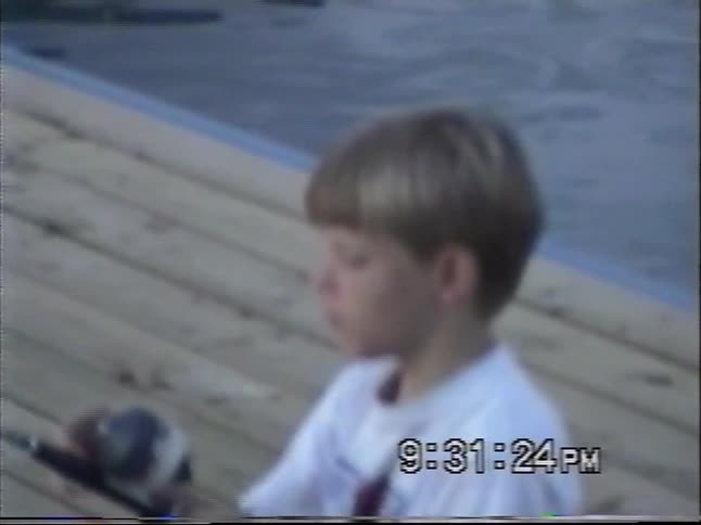 Vintage VHS footage captures two young boys fishing from a wooden dock in a marina at dusk