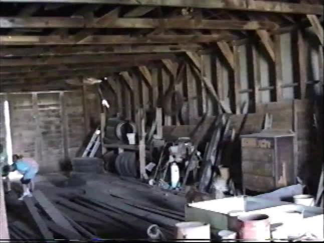 A slow panning shot reveals the cluttered interior of a rustic, old workshop filled with tools, furniture, and junk