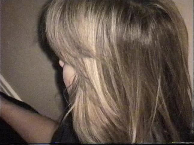 A woman gently pets her old black labrador retriever under the dining room table in this grainy vintage home video