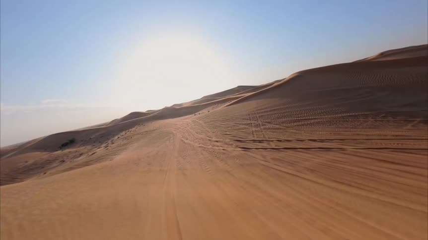 An exhilarating FPV drone flight swoops low over endless golden sand dunes under a clear blue sky