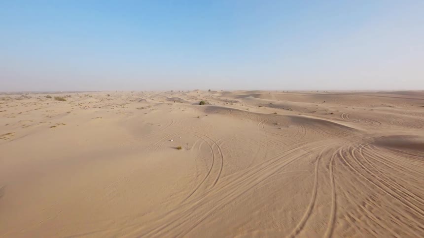 Aerial drone footage flies over a modern architectural building with a unique design and into the vast, sandy desert landscape