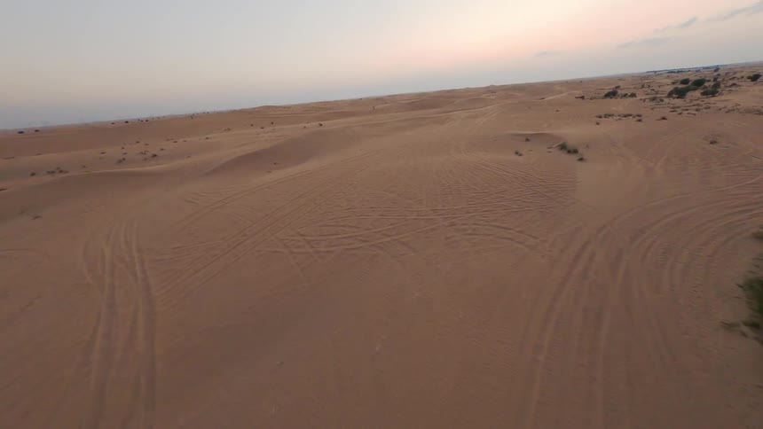 An FPV drone captures the striking modern architecture of a desert building before flying out over the vast sand dunes at dusk