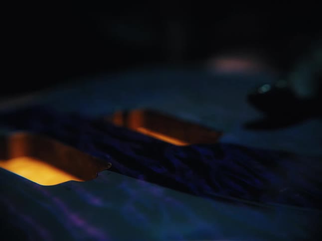 A luthier wearing a black glove slowly runs a hand over the beautifully finished blue and purple body of a custom electric guitar