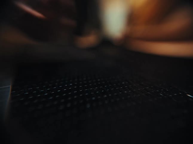 A shallow focus close-up shot of a tattooed hand picking up a precision craft knife from a dark, textured work surface